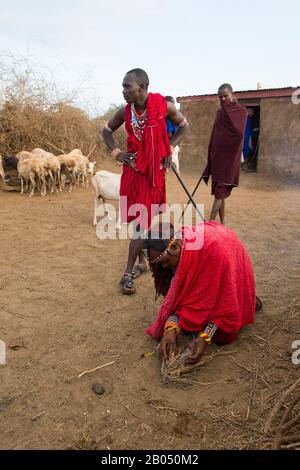 Scena del villaggio con uomini Masai che fanno un fuoco il modo tradizionale con un bastone di legno e frizione in un villaggio Masai fuori del Parco Nazionale Amboseli in K Foto Stock