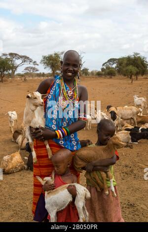 Villaggio con Masai donna e bambini che trasportano capre in un villaggio Masai fuori del Parco Nazionale Amboseli in Kenya. Foto Stock