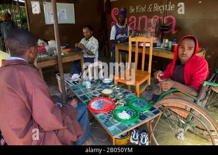 Persone disabili locali che fanno artigianato utilizzando materiali riciclati per il mercato all'ingrosso e al dettaglio dei consumatori presso la Shanga House di Arusha, in Tanzania Foto Stock