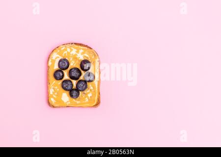 Sopra la vista di pane tostato al burro di arachidi con mirtillo in forma di cuore per colazione su sfondo rosa pastello con spazio copia Foto Stock