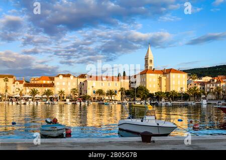 Supetar sull'isola di Brac vicino a Spalato, Croazia. Piccola cittadina di mare con passeggiata e porto con barche bianche, palme, caffè, case e chiesa. Touri Foto Stock