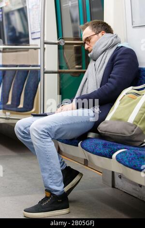 Uomo stanco in occhiali in metro treno. Giovane esausto maschio dormire in metropolitana dopo il lavoro, soft focus. Affaticamento cronico, concetto di privazione del sonno. Foto Stock