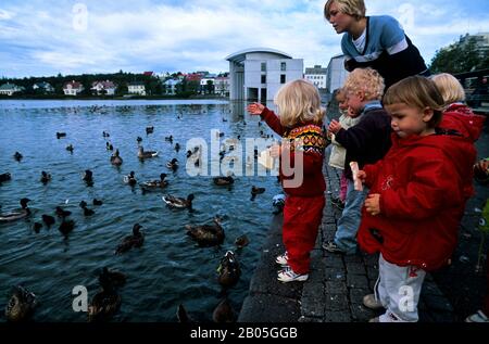 ISLANDA, REYKJAVIK, STAGNO DI TJORNIN, KINDERGARTENERS CHE ALIMENTA ANATRE Foto Stock