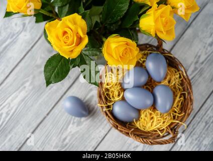 Uova di Pasqua in cestino e rose gialle vedere dall'alto Foto Stock