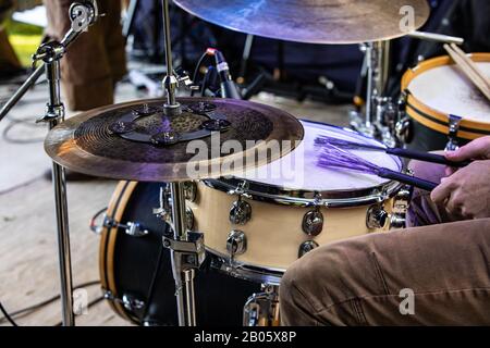 Una vista ravvicinata di un drum kit e delle gambe e delle mani di un batterista che suona sul palco. Durante una musica folk fissata a un festival di comunità alternative Foto Stock