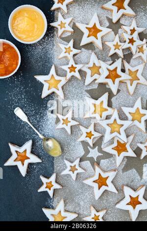 Biscotti Fatti In Casa Al Limone E Al Ponce Linzer. I biscotti sandwich con crema di limone e pesca preservano i biscotti a stella con zucchero a velo sulla pergamena e uno sfondo di ardesia Foto Stock