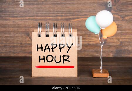 Happy Hour. Bar, ristoranti, negozio e vendita concetto. Notebook e palloncini colorati sullo sfondo di legno Foto Stock