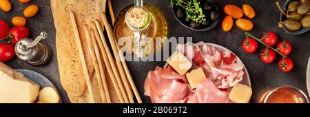 Cucina italiana panoramica shot, antipasti piatto lay. Prosciutto, formaggio, grissini, olive, sparati dall'alto su uno sfondo scuro Foto Stock