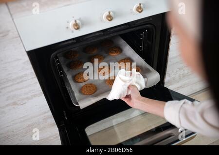 Mano femmina che prende fuori foglio di cottura dal forno. Foto Stock
