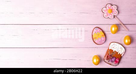 Banner di Pasqua festivo o biglietto di auguri. Uova dipinte di giallo, pan di zenzero colorato in forma di torta di Pasqua, fiore e uovo divertente su rosa toned legno b Foto Stock