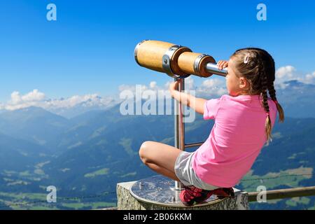 Ragazza che guarda attraverso un telescopio di legno, percorso panoramico cima della Salve Hohe, Hopfgarten, Brixental, Alpi Kitzbuehel, Tirolo, Austria Foto Stock