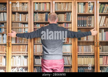 Uomo che cerca di afferrare la conoscenza dai libri sugli scaffali, Portogallo Foto Stock