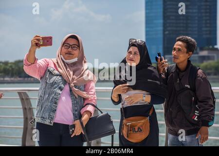 Tre turisti musulmani indonesiani in posa per una foto sotto il sole caldo nell'area di Merlion Park, Singapore Foto Stock