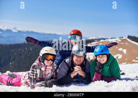 Felice famiglia di alpinisti, uomo, donna e ragazzi adolescenti in neve sul pendio di montagna sorridendo in macchina fotografica sullo sfondo di inverno boscosa montagne e cielo blu. Concetto di sport, viaggi e amicizia. Foto Stock