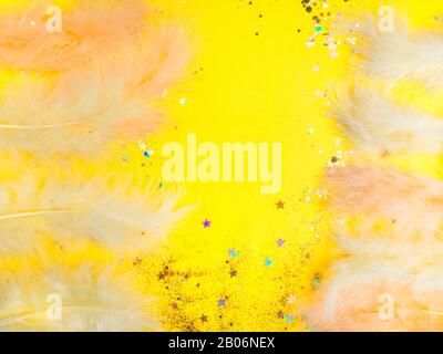 Pasqua giallo sfondo festivo con belle piume, glitter primavera concetto, copia spazio, vista dall'alto Foto Stock