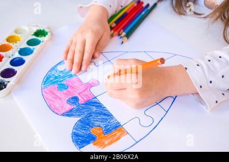 Un bambino sta disegnando cuore colorato con puzzle jigsaw su sfondo bianco come un simbolo di autismo, con matite colorate e acquerelli. Foto Stock