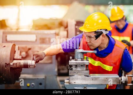 Tecnico asiatico che utilizza il calibro a corsoio per controllare la precisione delle dimensioni della macchina di servizio in fabbrica. Foto Stock