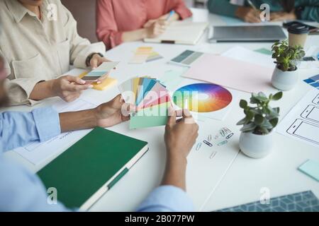 Primo piano dei progettisti seduti al tavolo scegliendo il colore dalla tavolozza colorata e discutendolo in team Foto Stock
