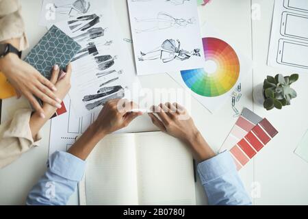 Primo piano di due colleghi che scelgono un colore e discutono gli schizzi per la loro nuova collezione di moda alla riunione Foto Stock