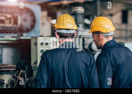 assistenza alla macchina parlare di lavoro di squadra lavorando in fabbrica nella vista posteriore. Foto Stock