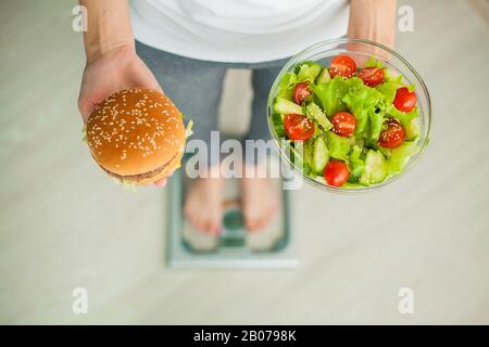 Concetto di dieta, bella giovane donna scegliendo tra il cibo sano e cibo spazzatura Foto Stock