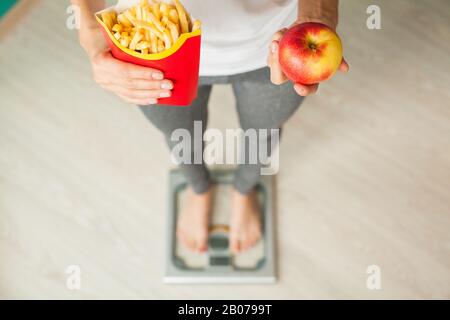 Concetto di dieta, bella giovane donna scegliendo tra il cibo sano e cibo spazzatura Foto Stock