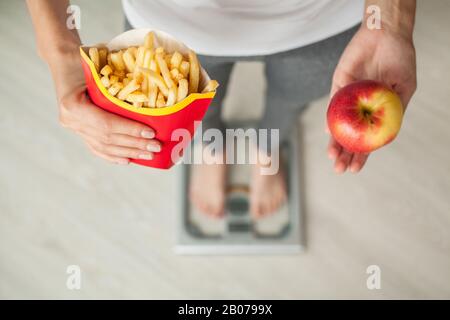 Concetto di dieta, bella giovane donna scegliendo tra il cibo sano e cibo spazzatura Foto Stock