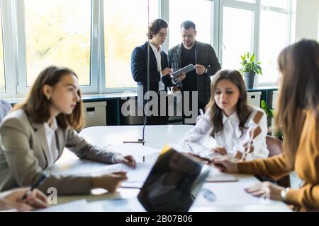 Un team esperto di progettisti grafici che si scambiano idee durante il processo di lavoro, creando una soluzione creativa e discutendo il concetto aziendale di successo, Foto Stock