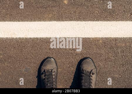 Esploratore urbano, uomo in scarpe moderne permanente sulla strada asfaltata con marcature bianche e spazio di copia Foto Stock