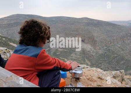 Il giovane coloni ebreo scaldando le mani su un vaso d'acqua che bolle su un bruciatore a gas nel canyon del fiume Nahal Arugot a Gush Etzion un gruppo di insediamenti ebraici situati nei Monti Judaei nella Cisgiordania Israele Foto Stock