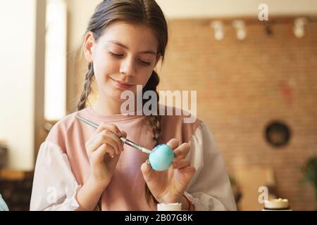 Cute ragazza pittura un uovo con le vernici che si prepara per la Pasqua Foto Stock