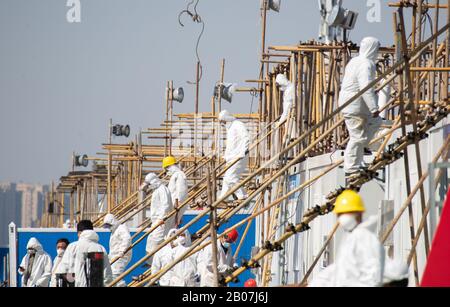 I lavoratori cinesi che indossano maschere facciali e indumenti protettivi si trovano nel cantiere dell'ospedale di Wuhan Leishenshan, utilizzato per il ricovero ospedaliero Foto Stock