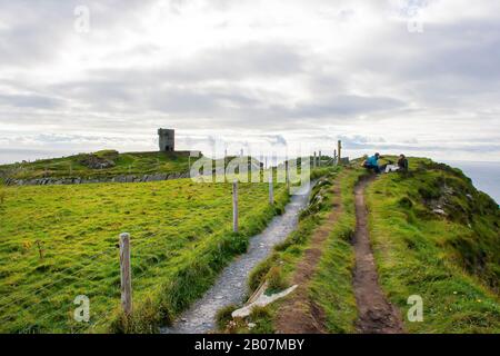 I turisti che si rilassano sulla pista sterrata alle scogliere di Moher a Co Clare nell'Irlanda occidentale sono stati portati in una giornata travolgente. Queste scogliere sono impressionanti Foto Stock