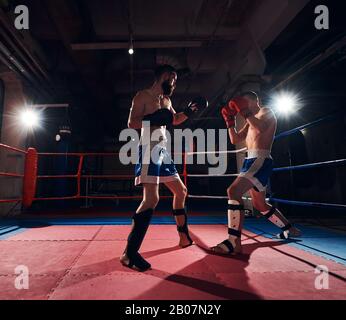 Due pugili maschili sportivi allenano il kickboxing nel ring del club benessere Foto Stock