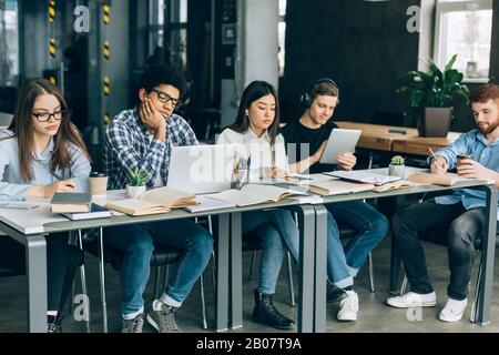 Studenti in biblioteca. Anni dell'adolescenza stanchi che fanno i compiti Foto Stock