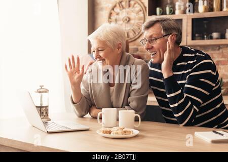 Felice senior coppia che guarda il notebook schermo in cucina e sventolare Foto Stock