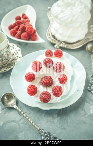 Deliziosa mini torta di meringa Pavlova decorata con lamponi freschi, con una bella tazza sdraiata su un piatto. Foto Stock