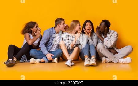Gruppo di amici multirazziali pettegolezzi su sfondo giallo Foto Stock