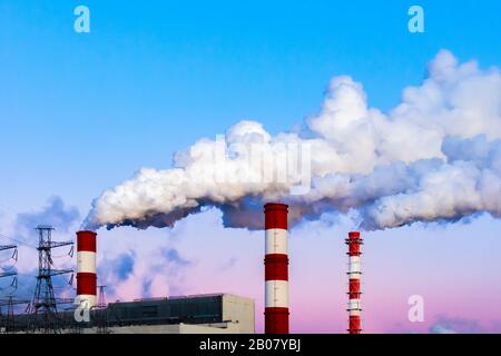 I camini della fabbrica inquinano l'aria, il fumo sporco denso, il cielo del crepuscolo serale. Bellissimo paesaggio industriale, inquinamento ambientale, aria avvelenata Foto Stock