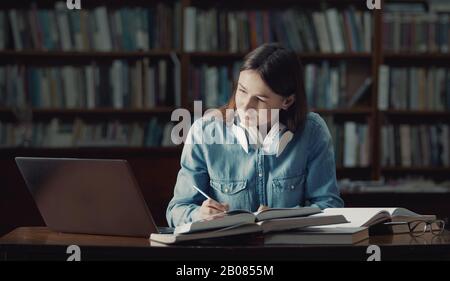 Giovane donna che studia in biblioteca Foto Stock