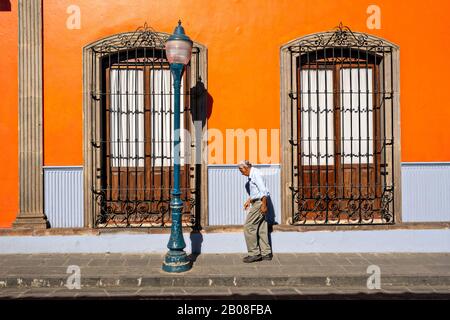 Un uomo anziano cammina attraverso un colorato edificio in stile coloniale nel centro storico quartiere di Coatepec, Stato Veracruz, Messico. Foto Stock