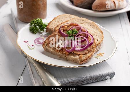Pane con lardo di maiale mescolato con crepitings macinati, decorato con anelli di cipolla viola e prezzemolo Foto Stock