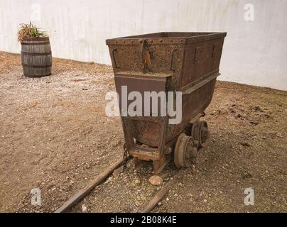 Un vecchio e arrugginito carro minerario su rotaie come decorazione nel giardino Foto Stock