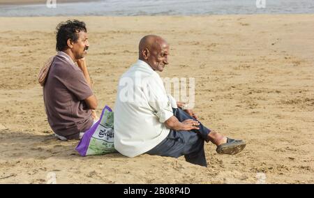 Due uomini indiani si siedono sulla spiaggia di Gokarna e stare all'oceano. Foto Stock