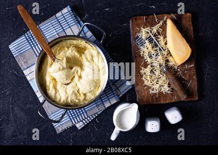 aligot, piatto di patate con purè di formaggio in una pentola di metallo con cucchiaio di legno su un tavolo da cucina in cemento, con ingredienti, cucina francese, vista orizzontale da Foto Stock