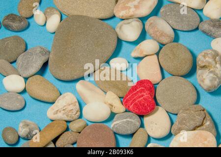 Pietra a forma di cuore rosso sullo sfondo blu di ciottoli di mare colorati Foto Stock