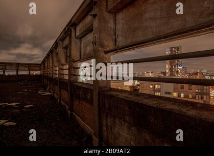 Inquadratura notturna incorniciata del centro della città di Leeds attraverso la parete a parapetto di un alto edificio Foto Stock