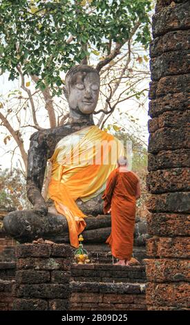 Un monaco buddhista in abito arancione prega davanti a una statua antica Foto Stock