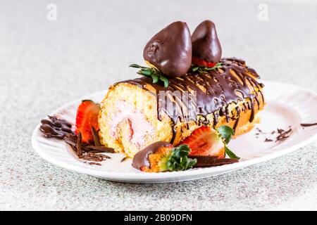 primo piano di un rotolo di torta alla vaniglia farcito con un mouse di fragola fresco e guarnito con fragole ricoperte di cioccolato Foto Stock