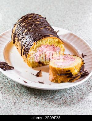 primo piano di un rotolo di torta alla vaniglia farcito con un mouse di fragola fresco e cioccolato fondente fuso sulla parte superiore Foto Stock